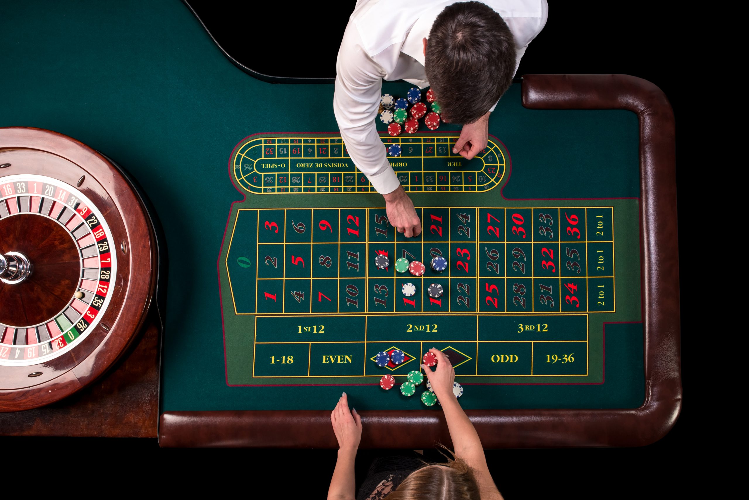 Man croupier and woman playing roulette at the table in the casino. Top view at a roulette green table with a tape measure.